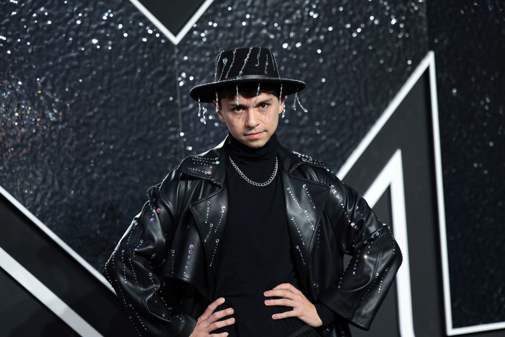 Mikey poses with their hands on hips against a textured, geometric backdrop