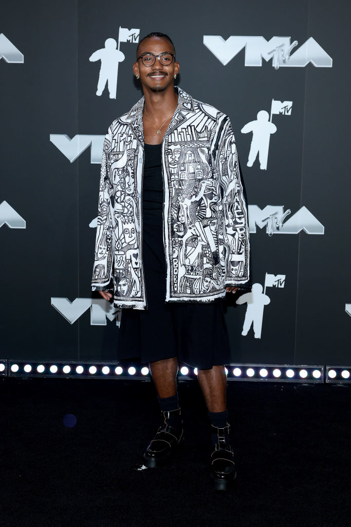 Yai Ariza at the VMAs wearing a patterned jacket, dark shirt, dark shorts, and dark boots