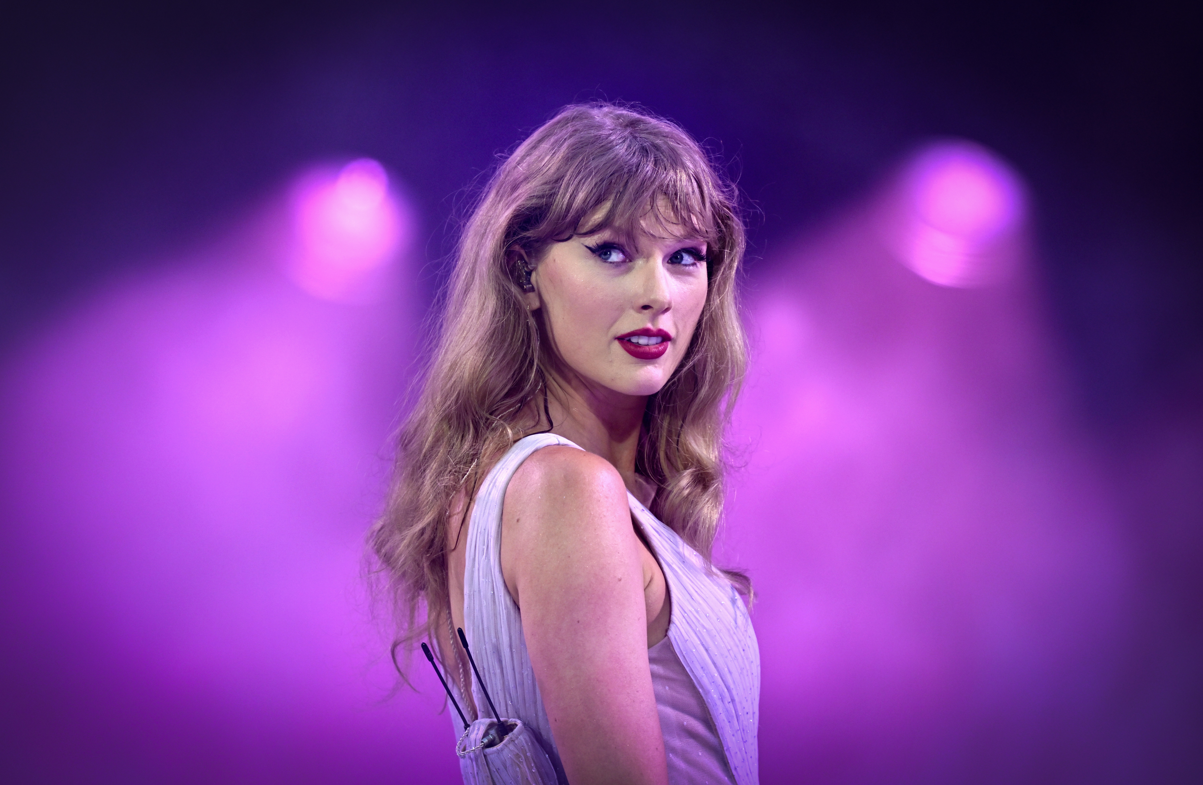 Taylor Swift on stage in a stylish sleeveless dress with a backdrop of purple lights