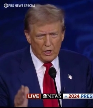 Donald Trump speaking at a 2024 presidential debate, wearing a suit and red tie