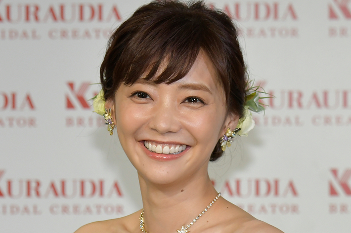 笑顔の女性が花模様のドレスを着てKURAUDIAのロゴが背景にあるイベントに登場。