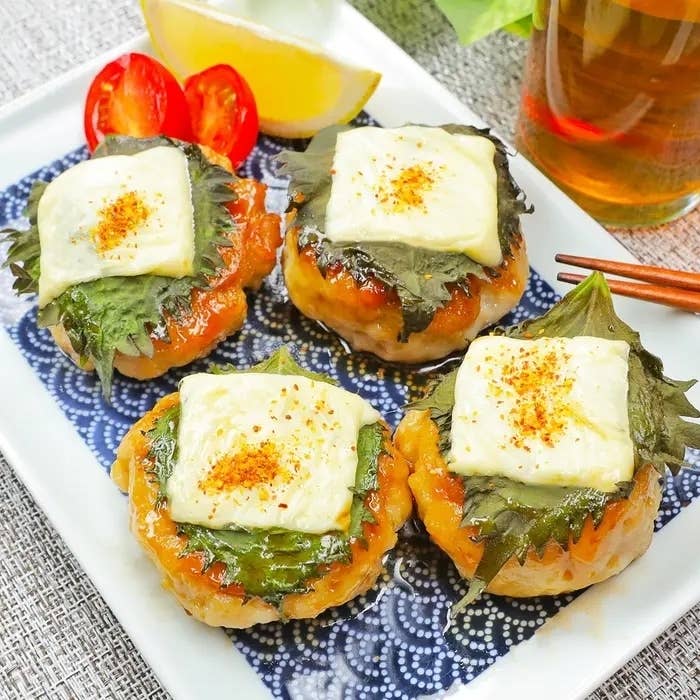 お皿に盛られた4つの鶏つくねを、大葉とチーズをのせて焼いた料理。横にミニトマトとレモンが添えられている。