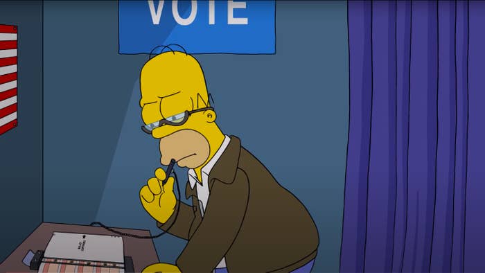 Homer Simpson in a voting booth, examining a ballot with a pensive expression. An American flag is visible in the background