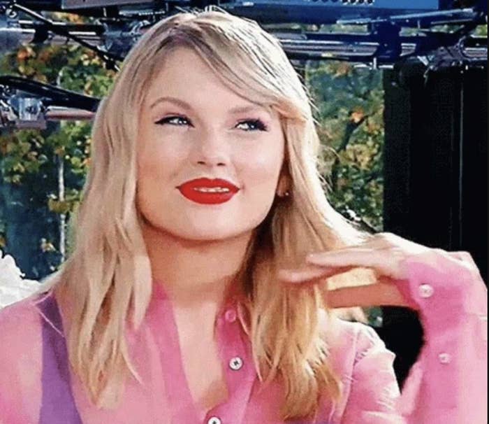 Taylor Swift smiling, wearing a button-up blouse with long, wavy hair