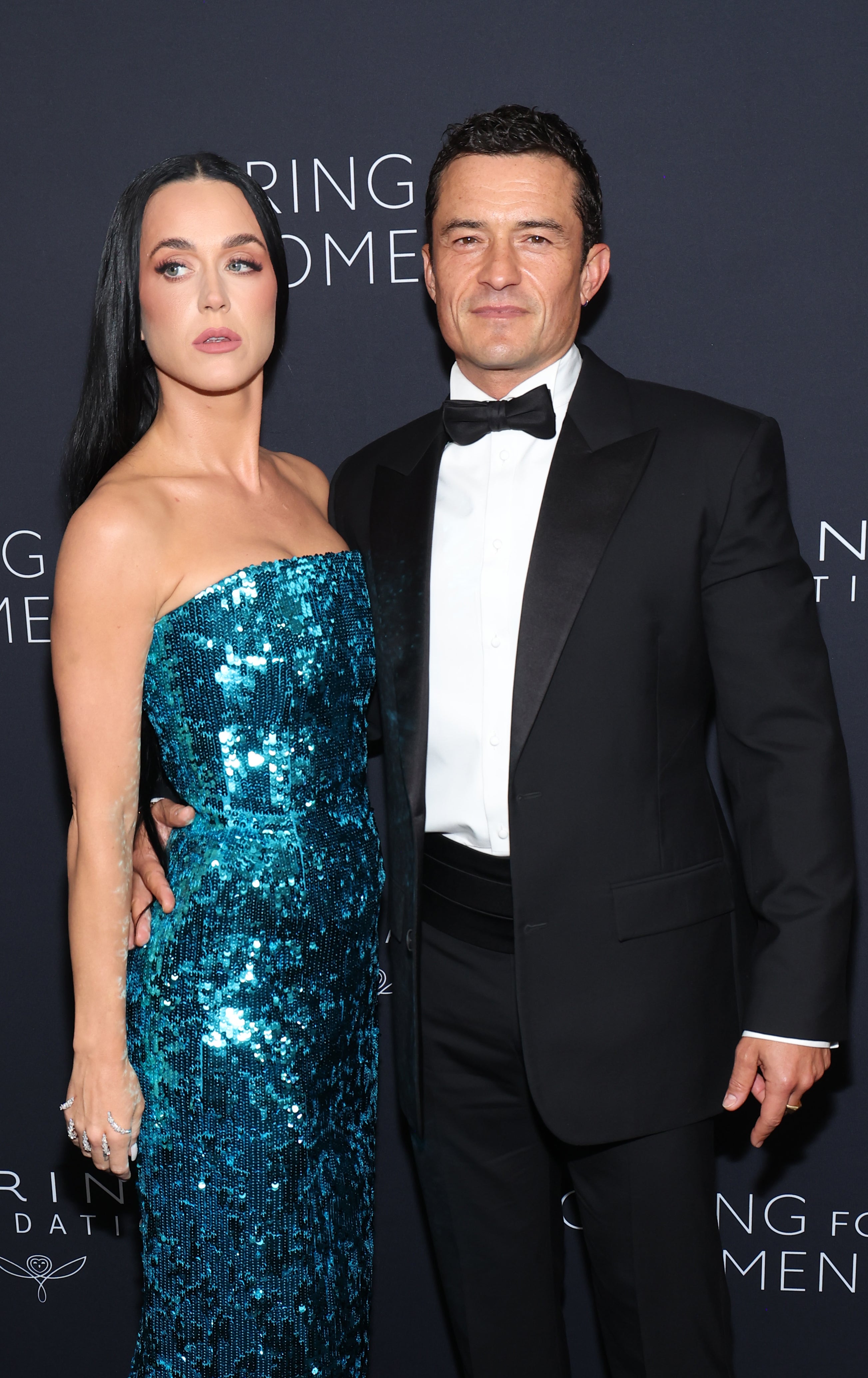 Katy Perry, in a sparkly strapless dress, poses with Orlando Bloom, in a black tuxedo, at a formal event