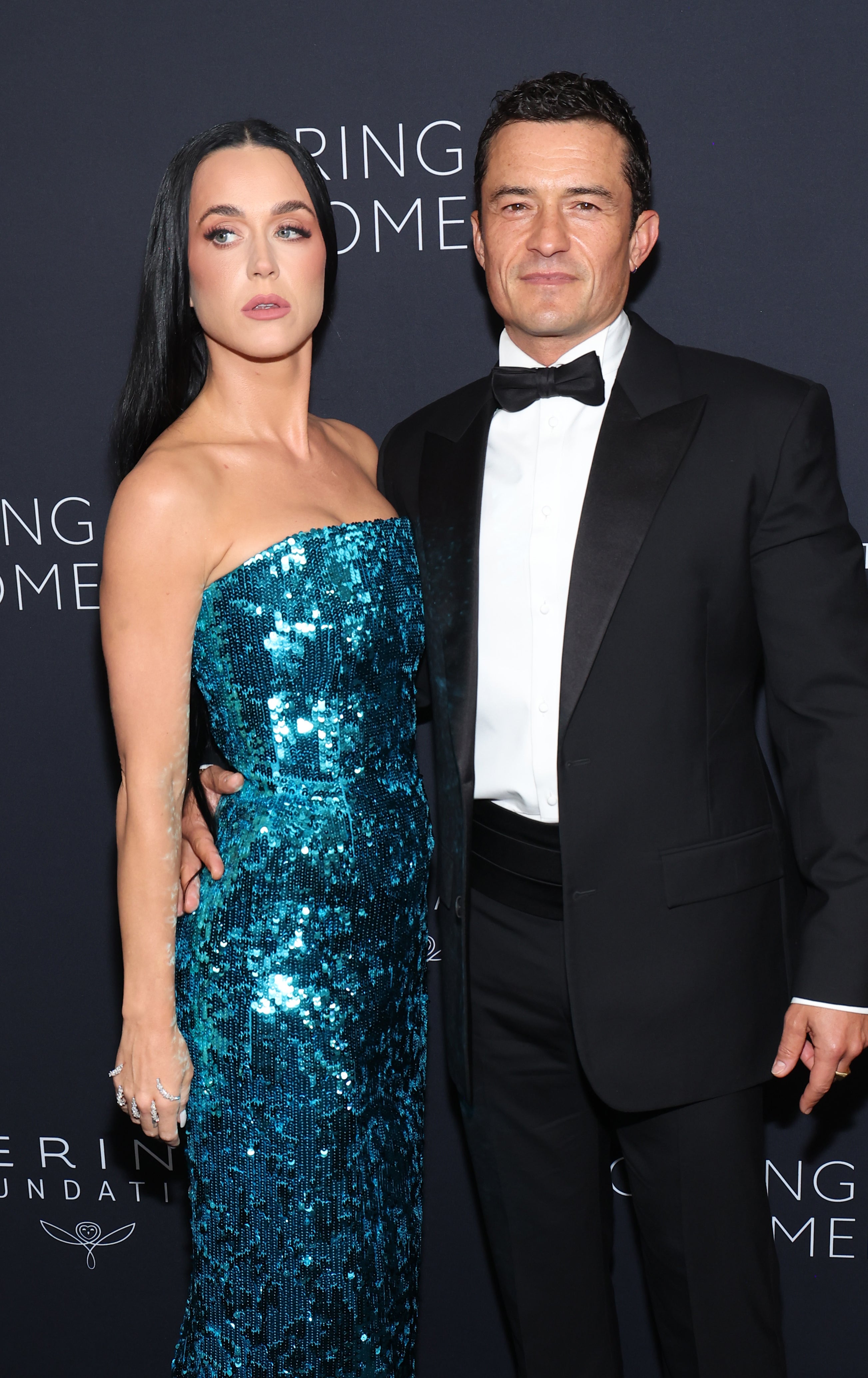 Katy Perry, in a sparkly strapless dress, poses with Orlando Bloom, in a black tuxedo, at a formal event