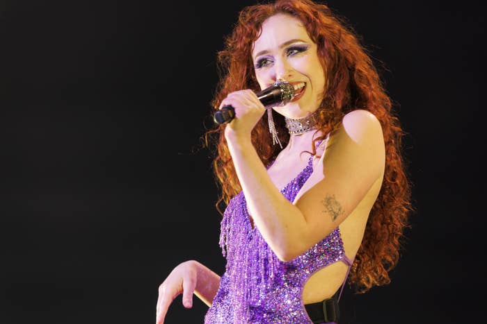 Chappell Roan with long curly hair sings into a microphone on stage, wearing a sparkling, sequin-fringe dress