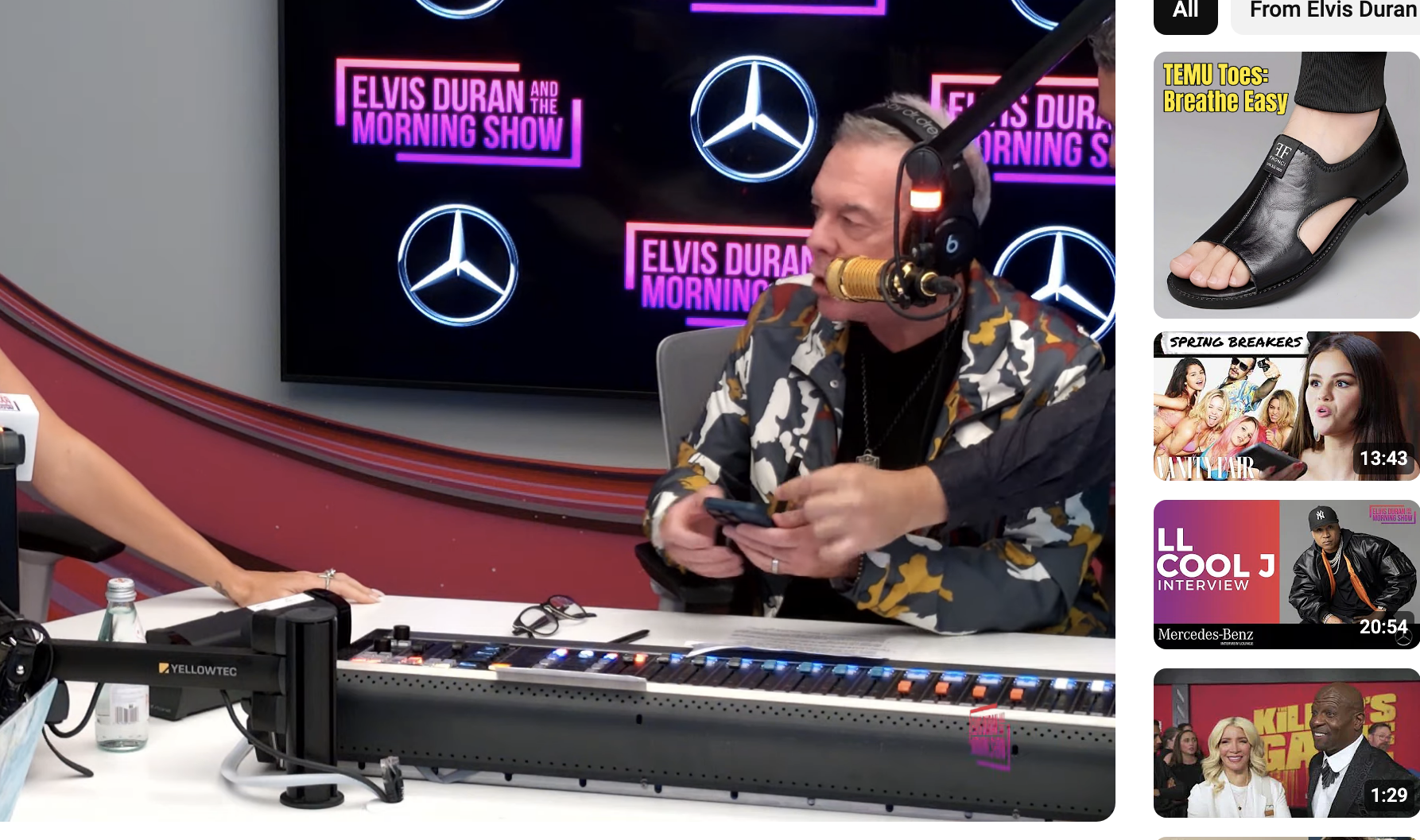 Katy Perry and a host converse in a radio studio during the Elvis Duran Show. The background features microphones and screens with the show&#x27;s logo