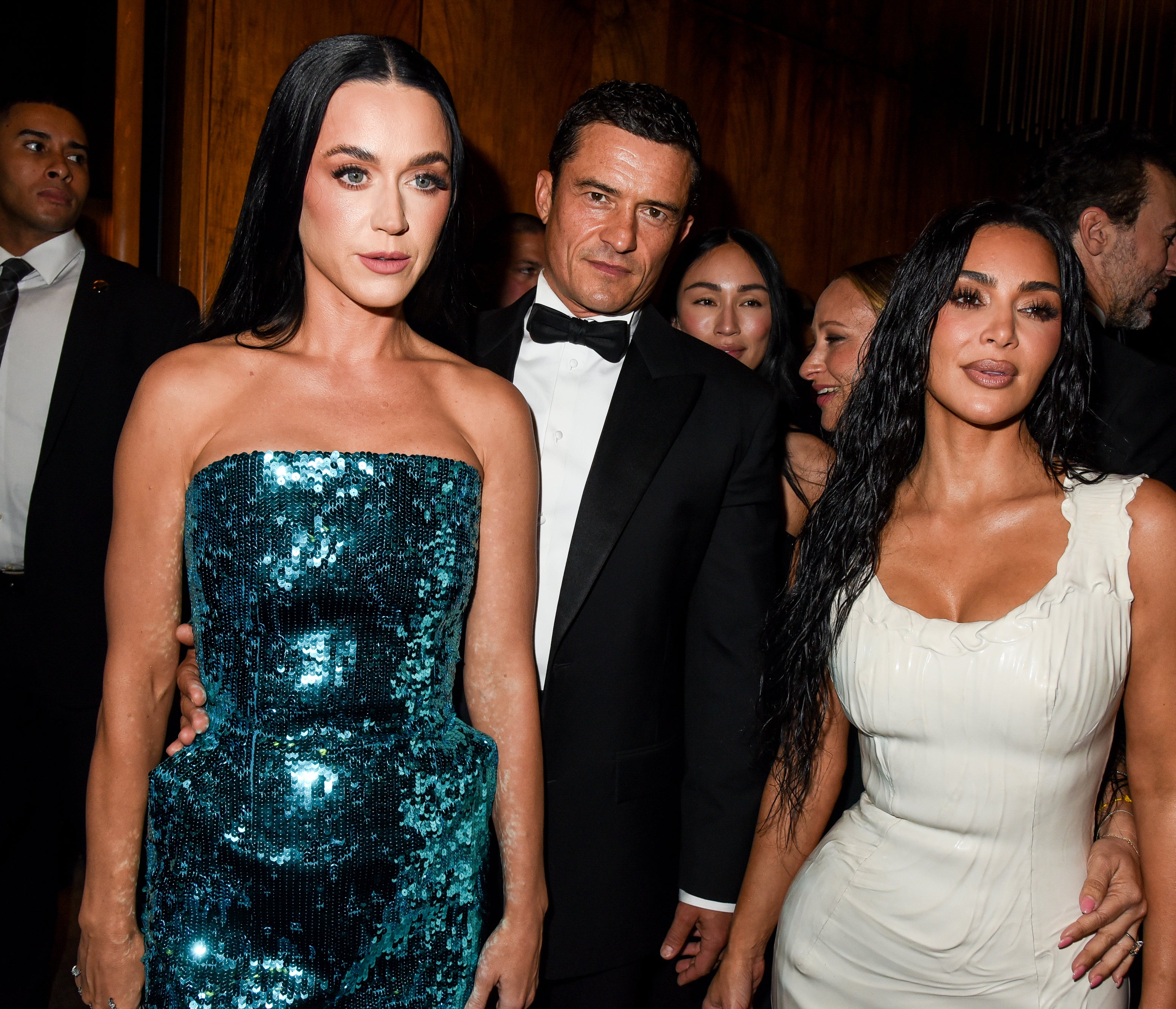 Katy Perry in a sequined dress, Orlando Bloom in a tuxedo, and Kim Kardashian in a form-fitting dress pose together at an event