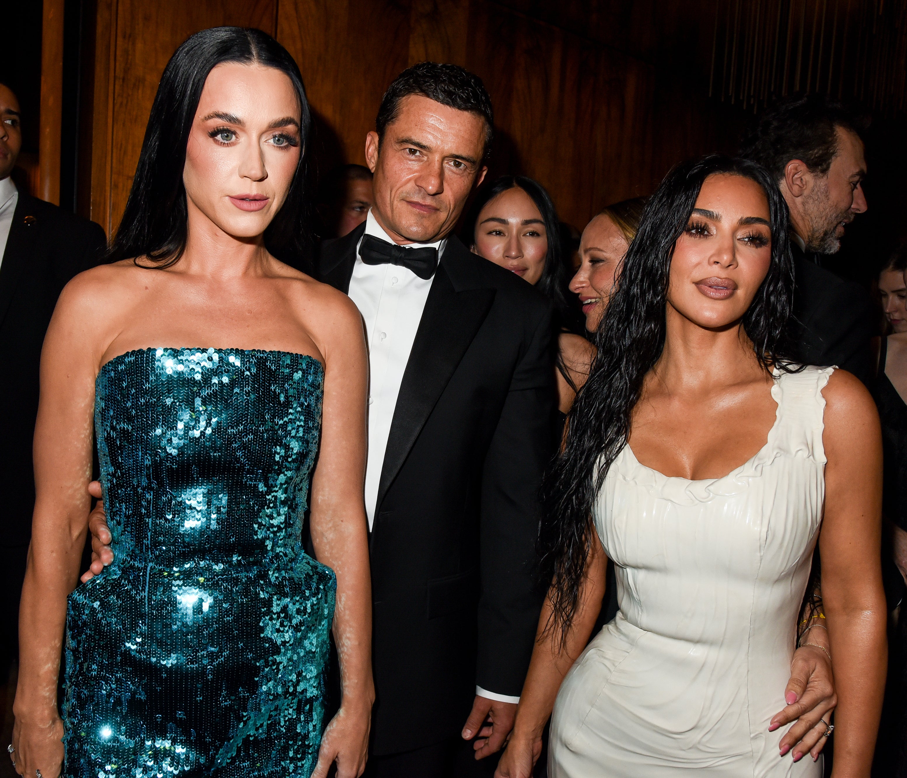 Katy Perry in a sequined dress, Orlando Bloom in a tuxedo, and Kim Kardashian in a form-fitting dress pose together at an event
