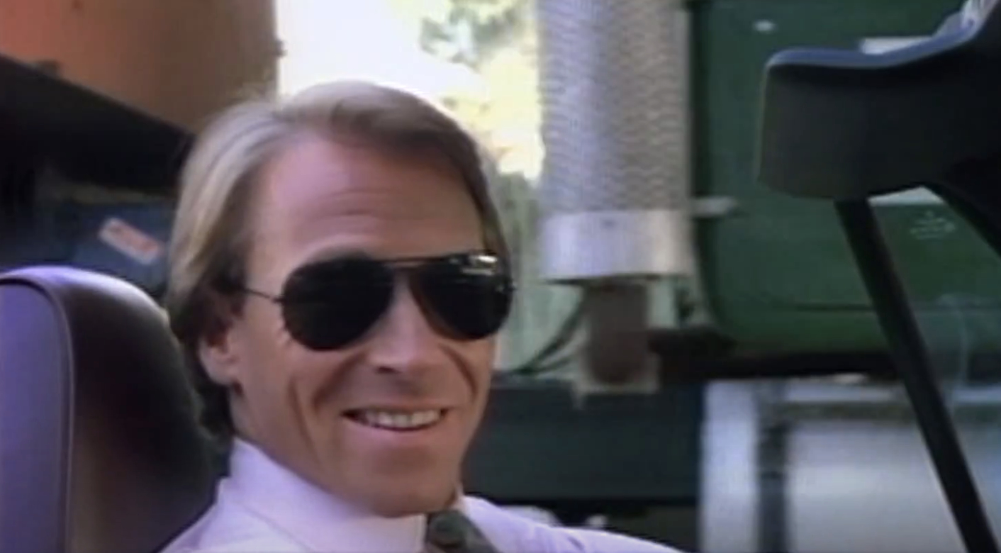 Man in aviator sunglasses smiling while seated in a vehicle