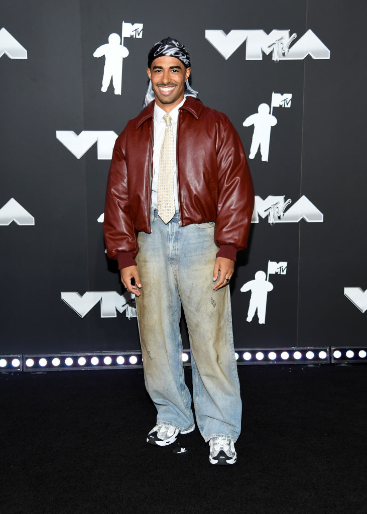 Boman at the VMAs, wearing a leather jacket, loose-fitting jeans, and sneakers, with a bandana