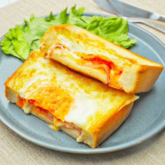 チーズとハムが挟まれたホットサンドが半分に切られて皿に盛られている。隣にレタスが添えられている。