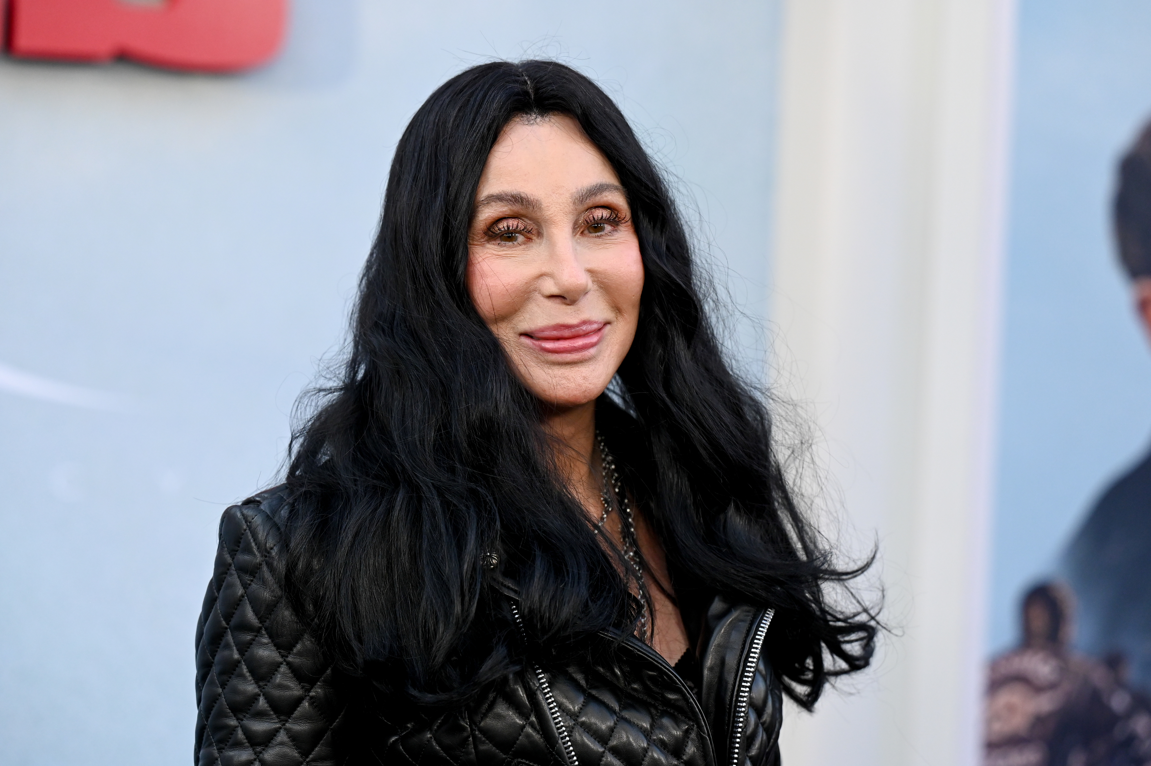 Cher smiles at the camera while wearing a black quilted jacket