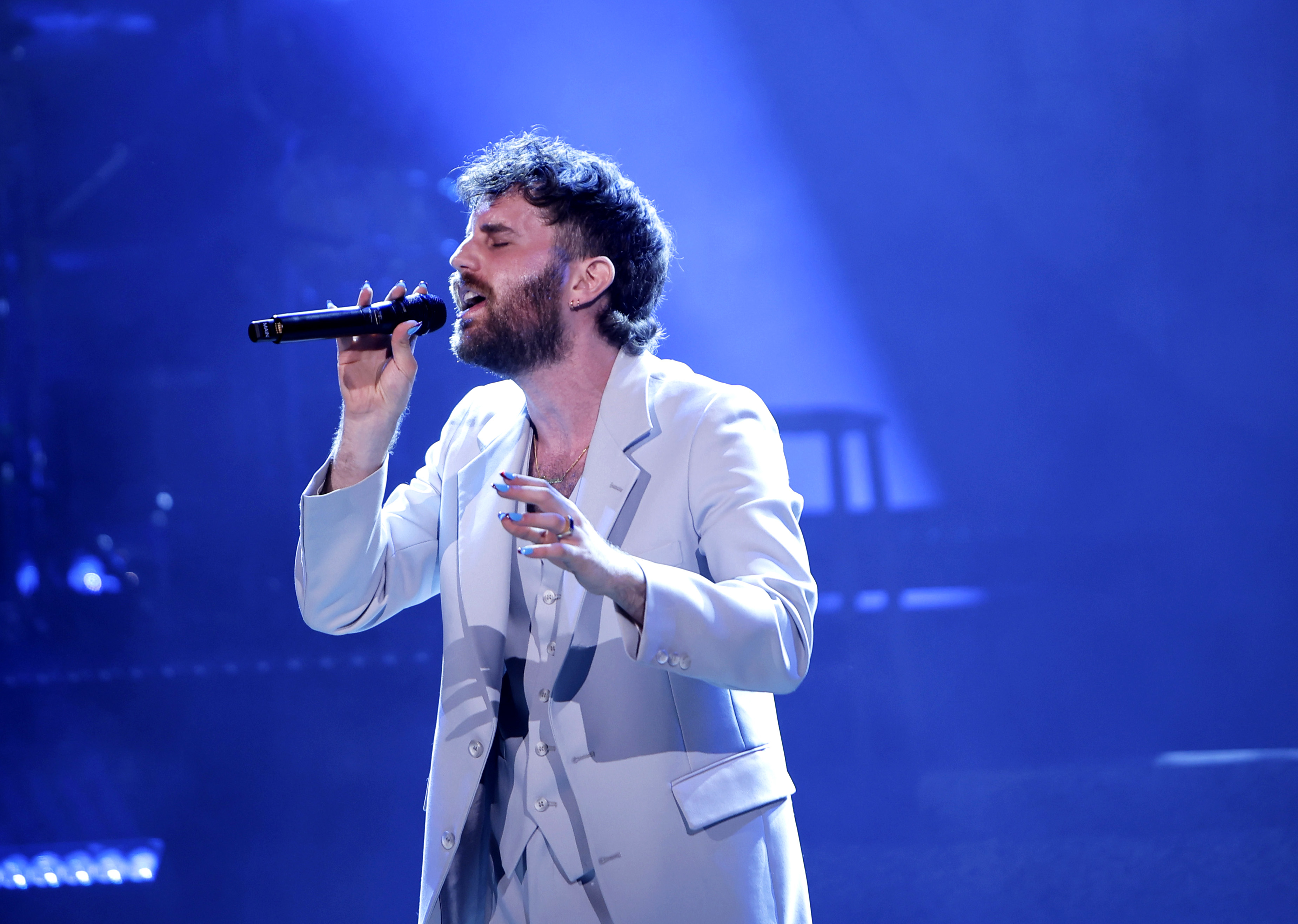Ben Platt sings passionately on stage, wearing a light-colored suit during a live performance