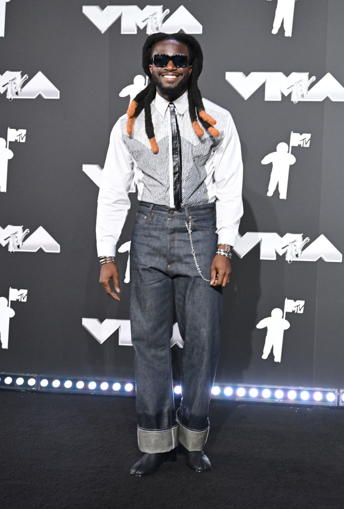 Shaboozey in a checkered shirt, dark jeans, and sunglasses poses on the MTV VMA red carpet