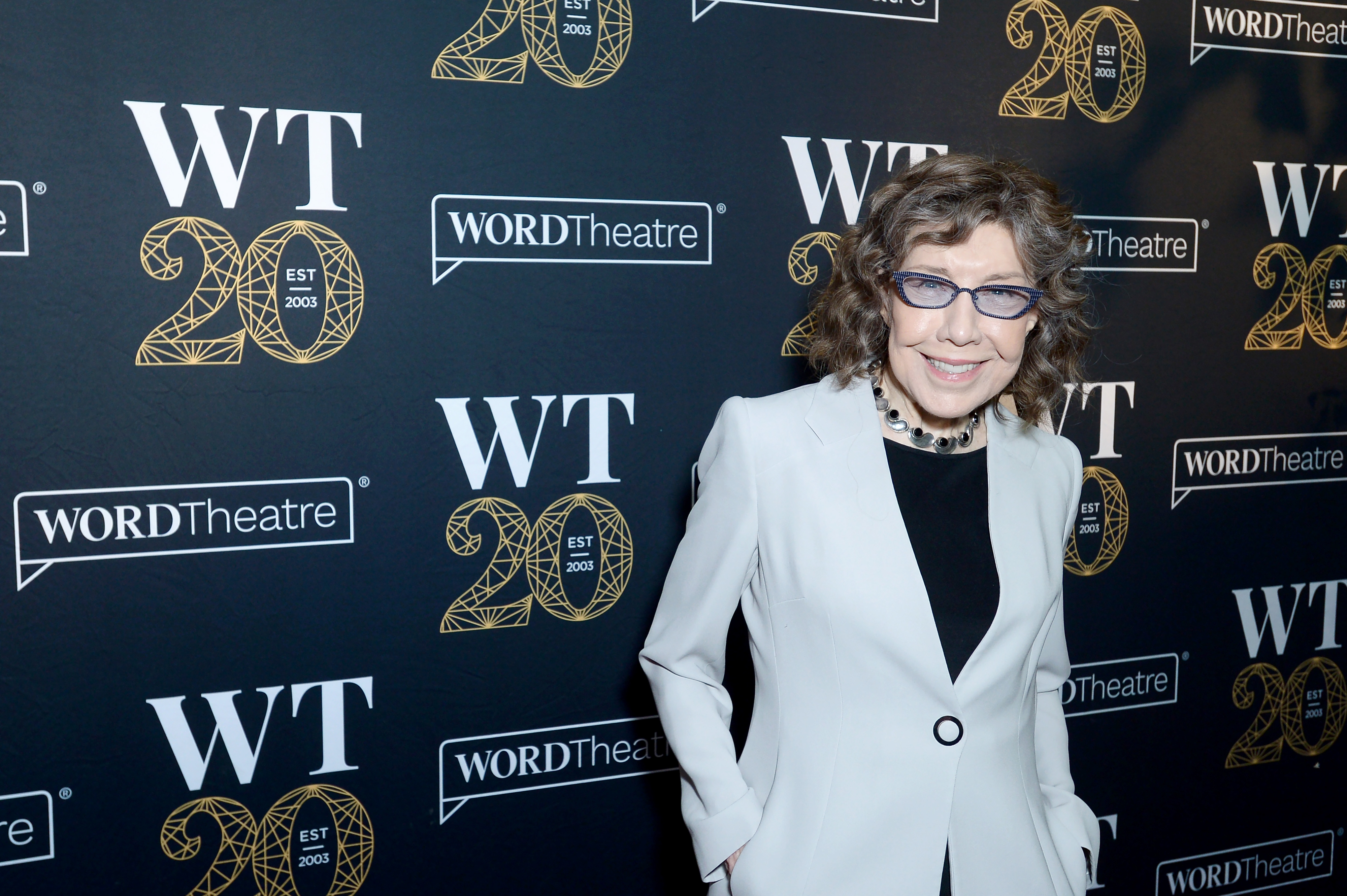 Lily Tomlin smiles on the red carpet at the WORDTheatre 20th anniversary event, wearing a white blazer over a black top