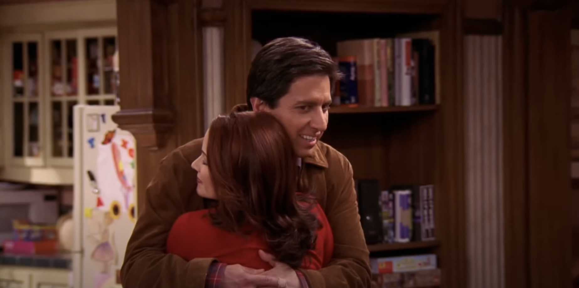 Ray Romano and Debra Messing hugging in a warmly lit living room