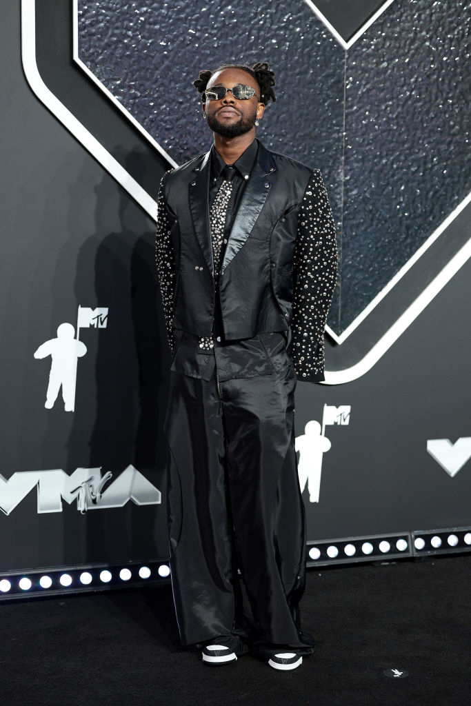 Lojay poses on the red carpet at the VMAs wearing a dark, textured suit with patterned sleeves and a button-up shirt