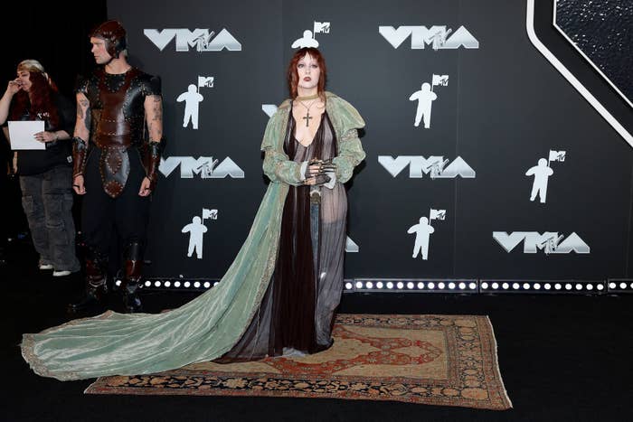 Chappell on the VMAs red carpet in an ornate, medieval-inspired gown with a long train, accompanied by a man in matching armor-like attire