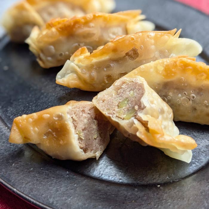 黒い皿の上に盛られた数個のギョーザー。中央のギョーザは半分に割れていて、中の具材が見えている。
