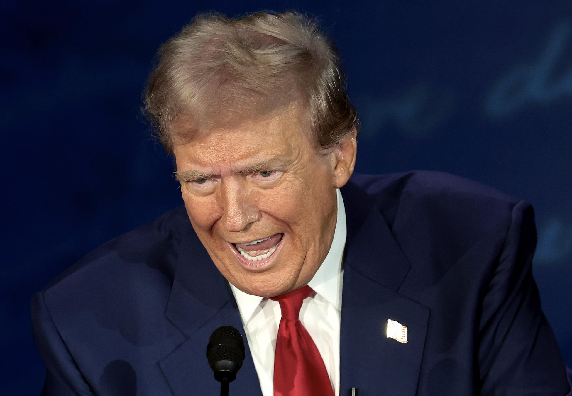 Donald Trump speaks into a microphone at an event. He is wearing a suit and tie