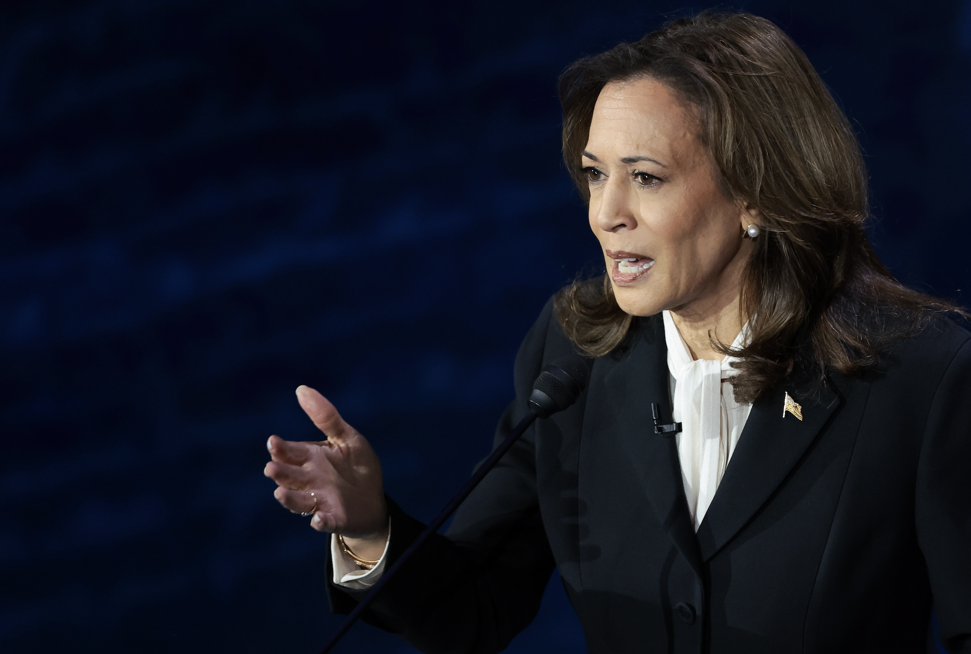 Kamala Harris speaks passionately with one hand raised while wearing a suit jacket over a shirt