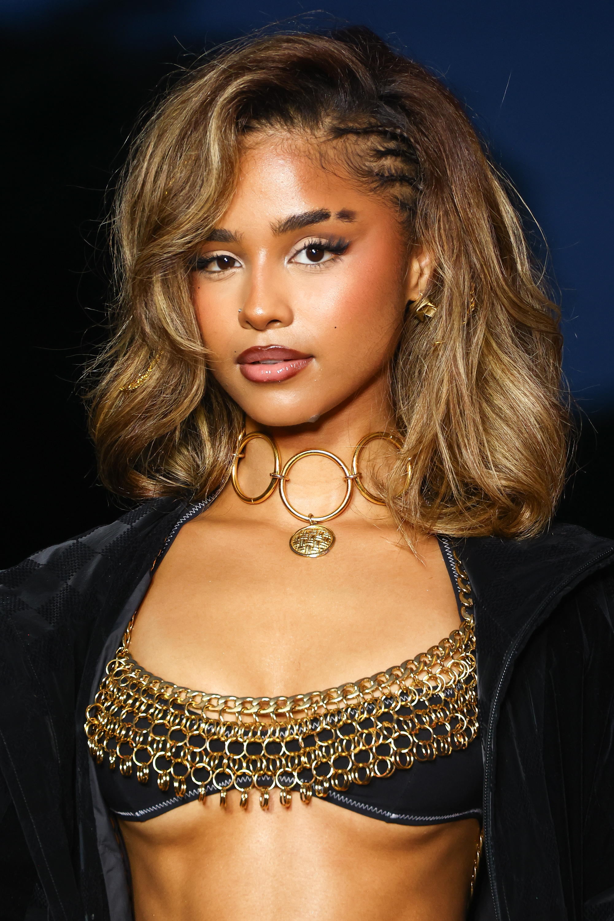 Tyla with shoulder-length wavy hair wears a chain-link top and jacket