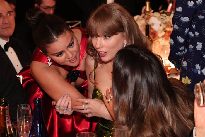 Selena Gomez and Taylor Swift engage in an animated conversation at a formal event, joined by a third unidentified person