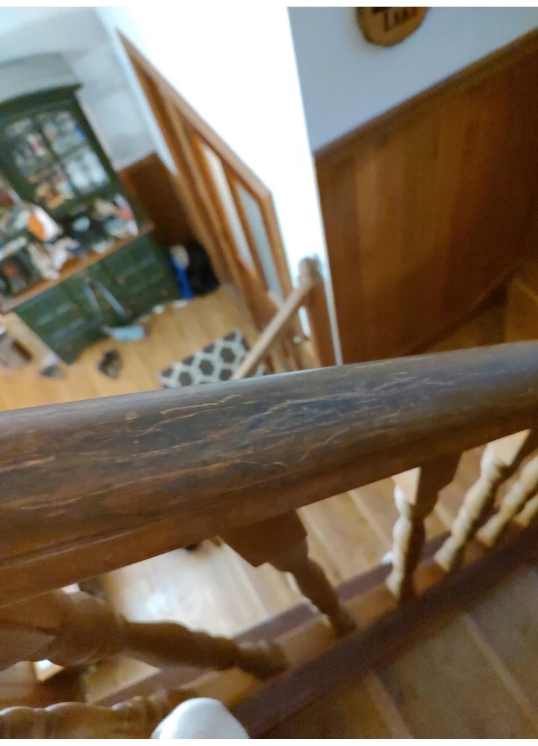 View from a staircase, showing a railing in the foreground and a cluttered room with shelves and various items in the background. No people are visible