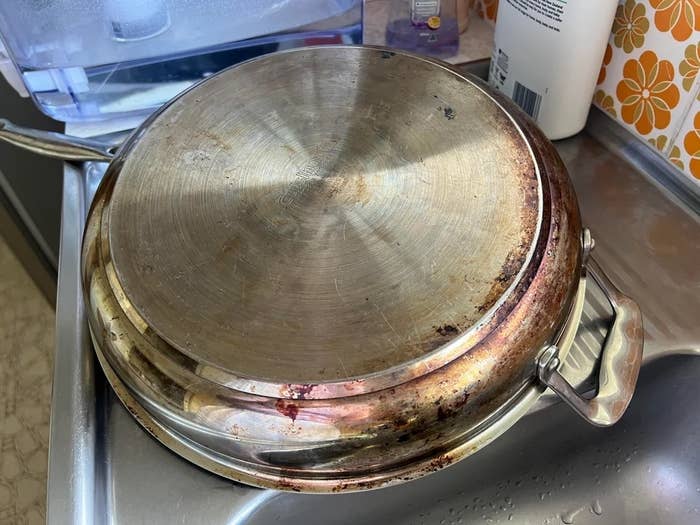 A used copper bottom frying pan with visible stains and scratches is placed upside down on a kitchen countertop. Nearby are various kitchen items