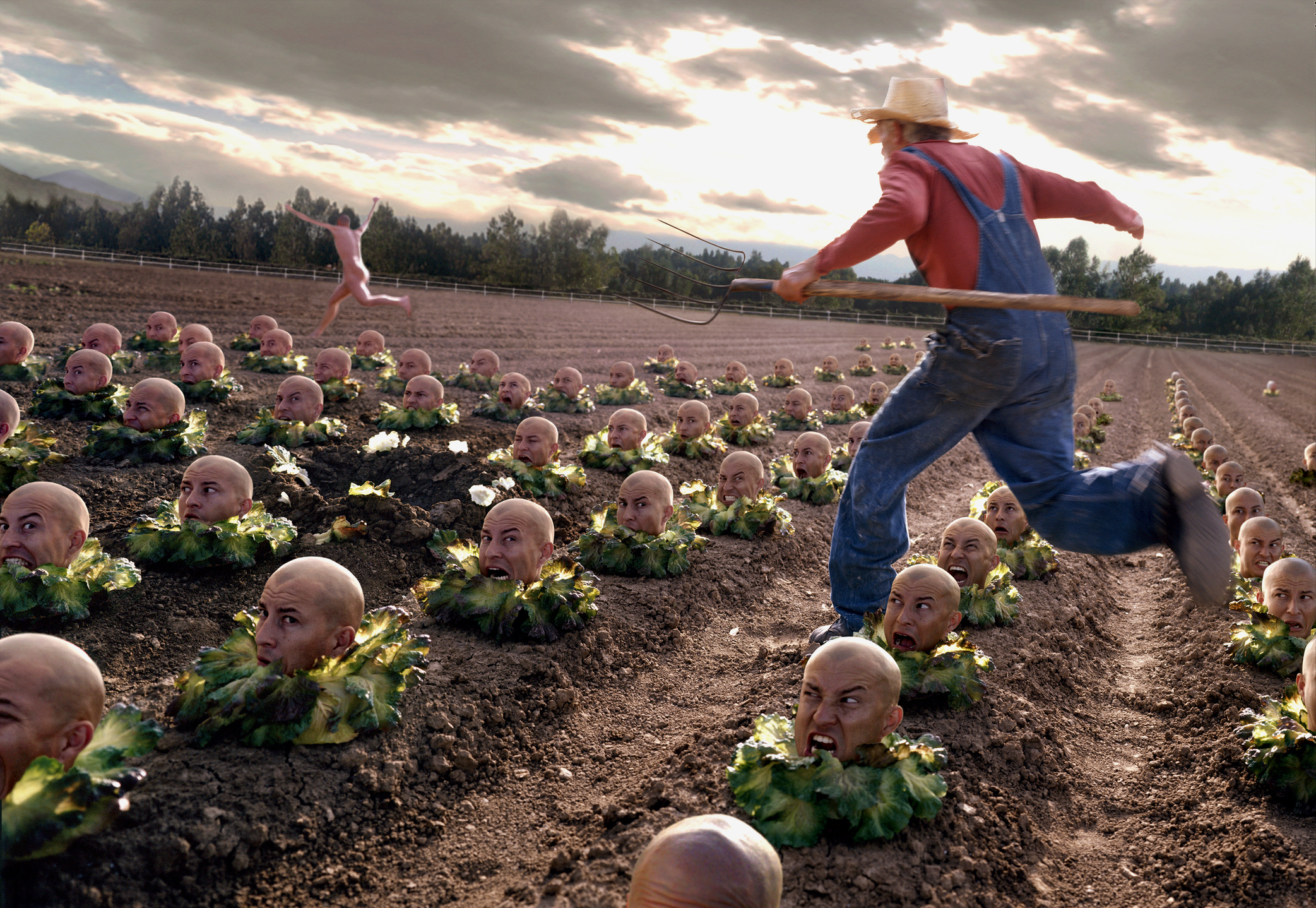 A farmer in overalls and a straw hat jumps through a field of cabbages, each with a human head, against a backdrop of trees and cloudy sky