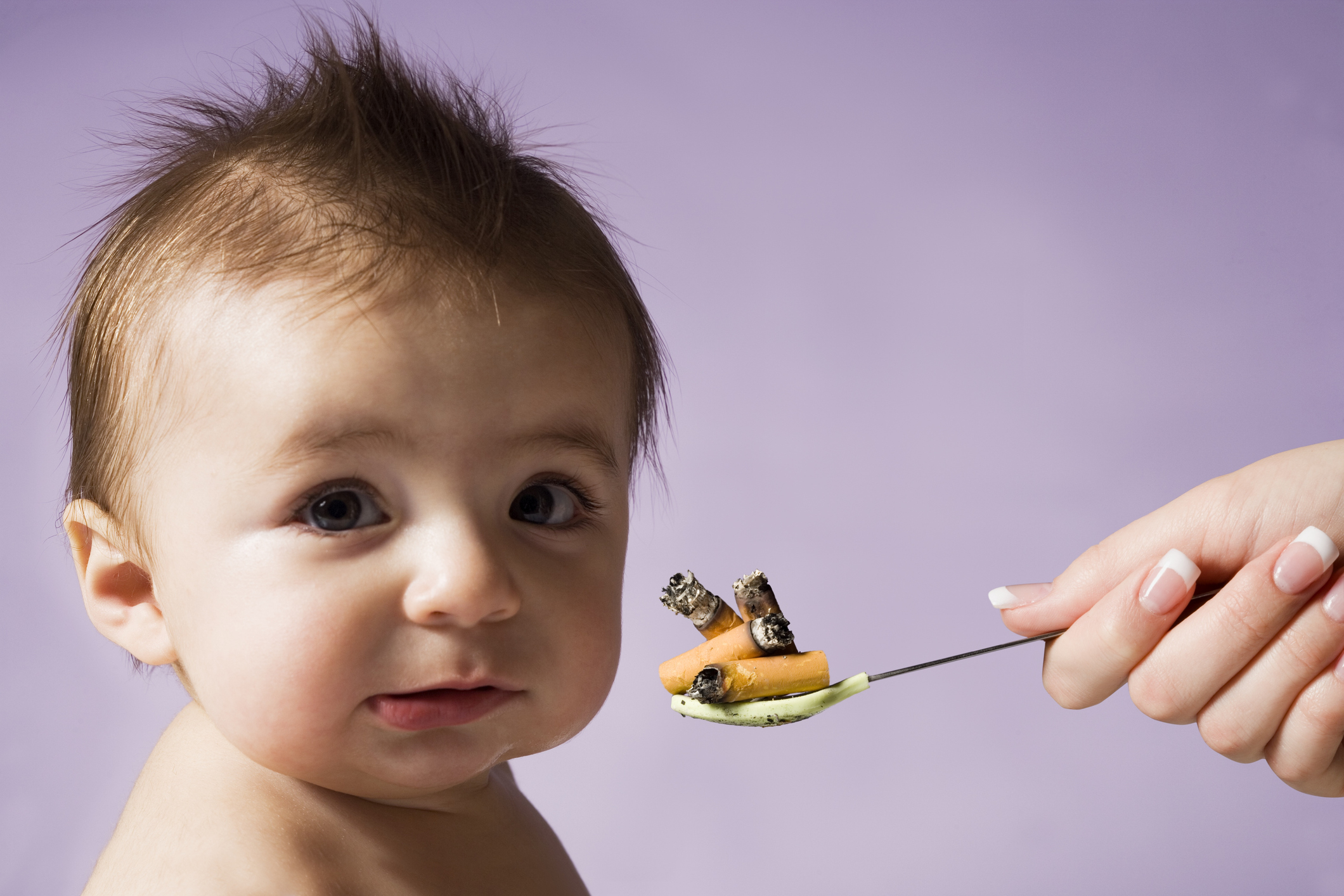 A baby looks at the camera while a hand holding a spoon with cigarette butts is close to the baby's face
