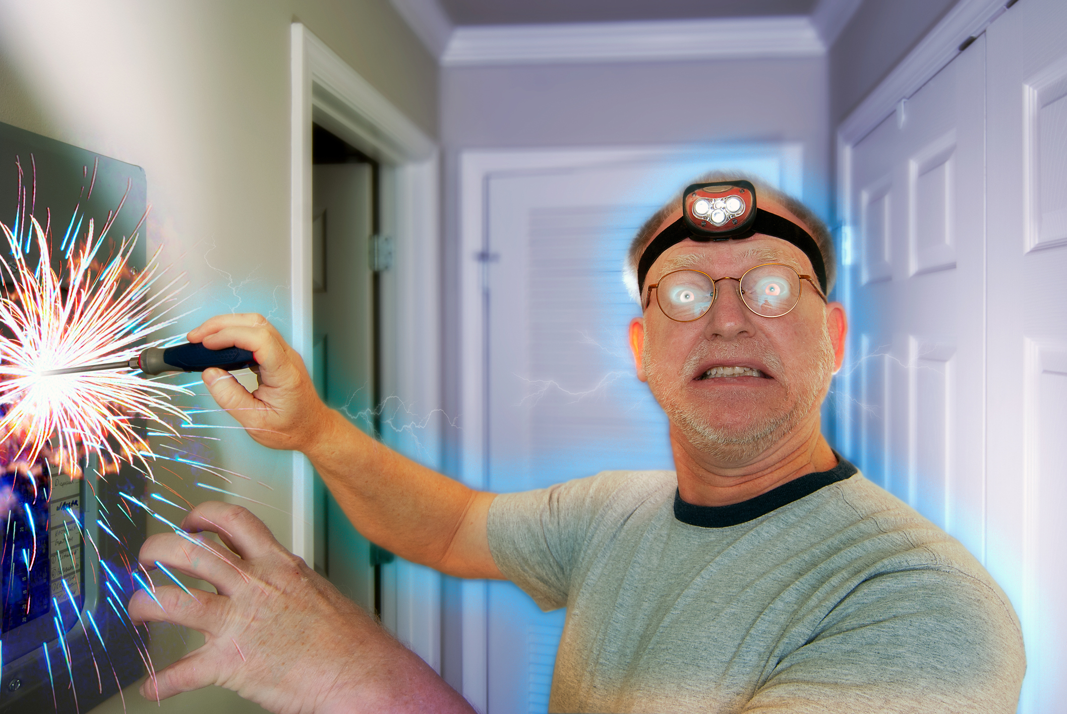 A man wearing a headlamp and glasses is shocked while using a screwdriver on an electrical panel, causing sparks
