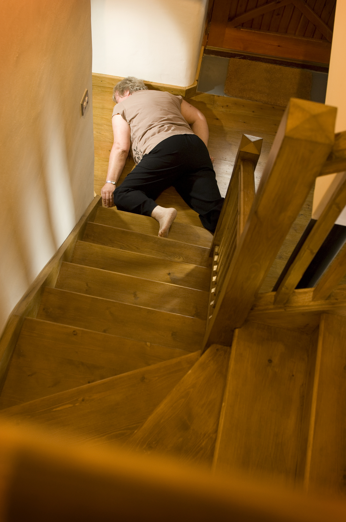 A person lies face down on wooden stairs, appearing to have fallen. The setting is indoors without any visible assistance nearby