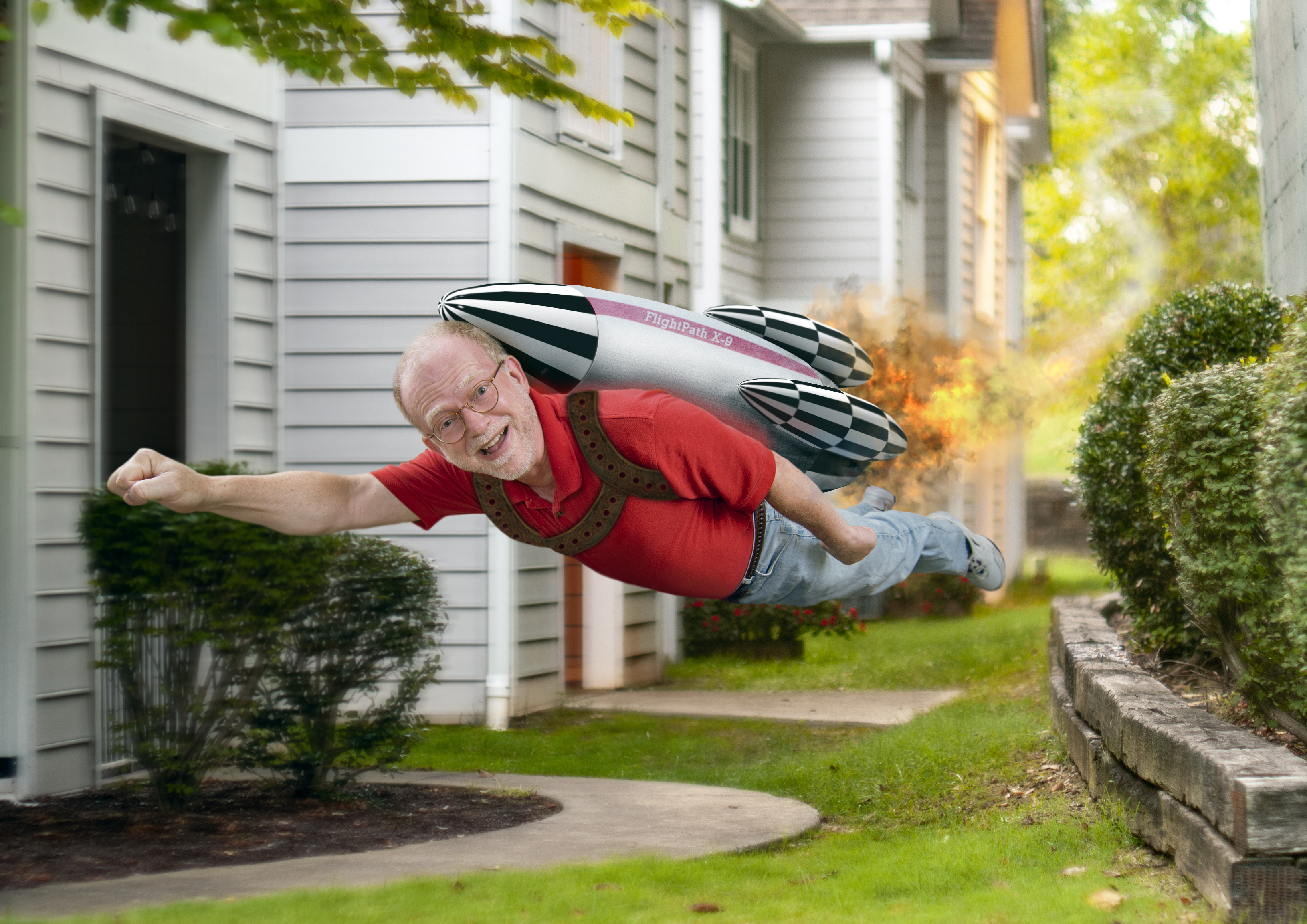 Elderly man wearing a red shirt and jeans, smiling mid-flight via a mock jetpack. Residential neighborhood background with greenery