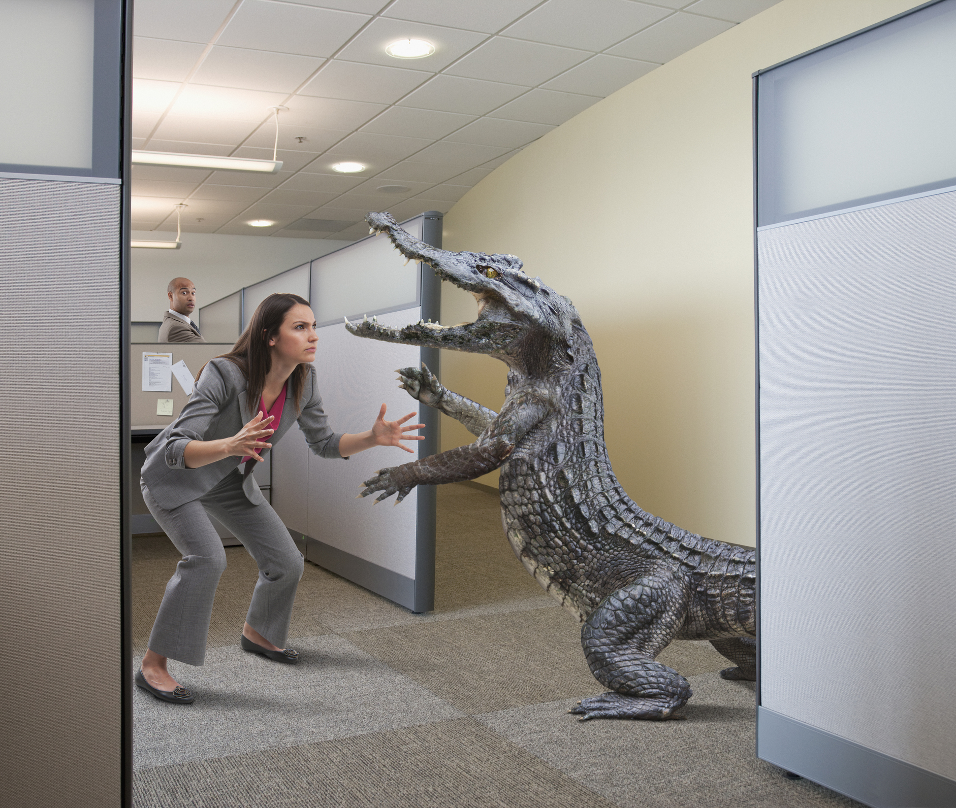 A woman in office attire faces a large, menacing alligator in a cubicle. A man in another cubicle looks concerned in the background