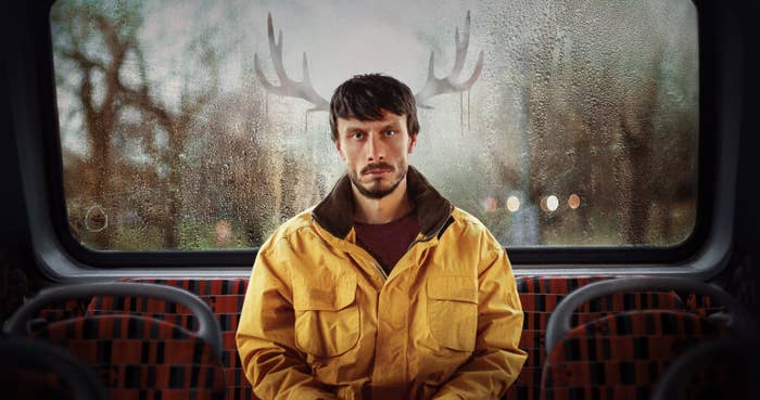 A man with a serious expression, seated on a bus with antlers seemingly growing from his head, created by the condensation on the window behind him