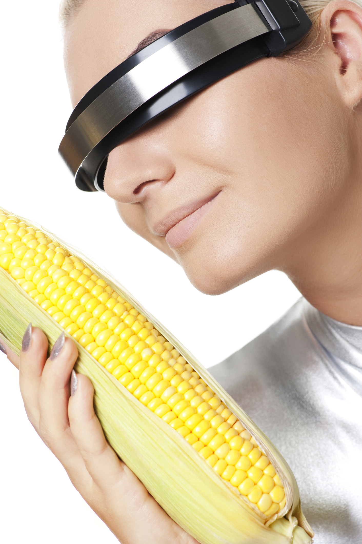 Person wearing a metallic headband with a visor, holding an ear of corn close to their face