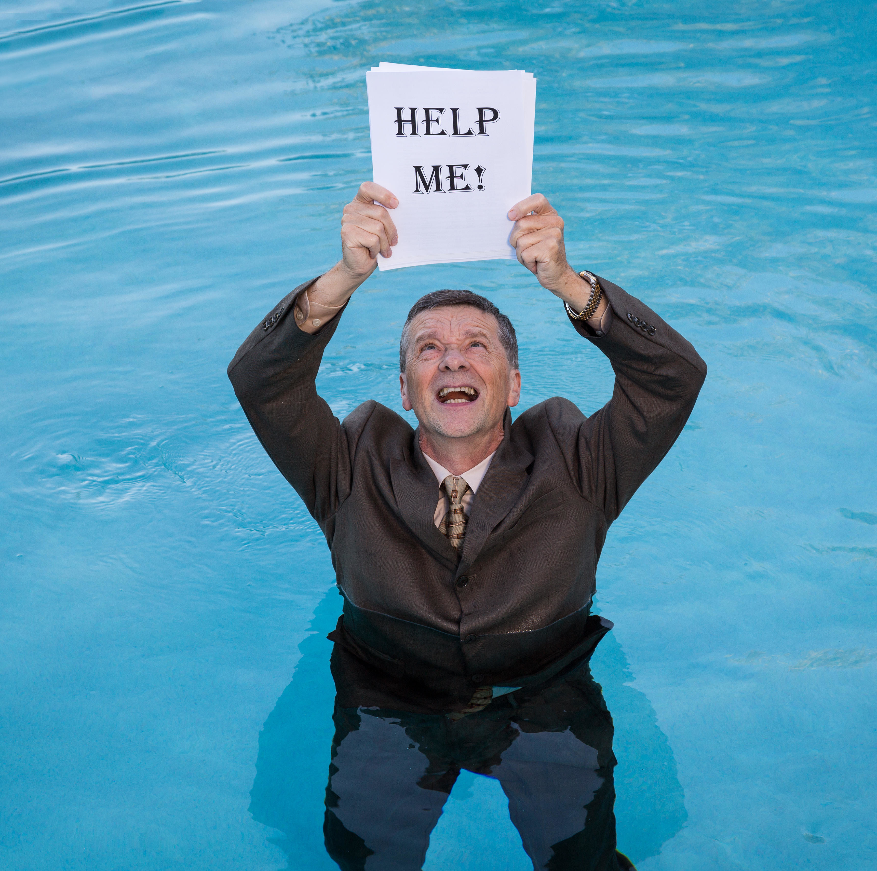 Man in a suit standing in a pool, holding papers above his head that say "HELP ME!"