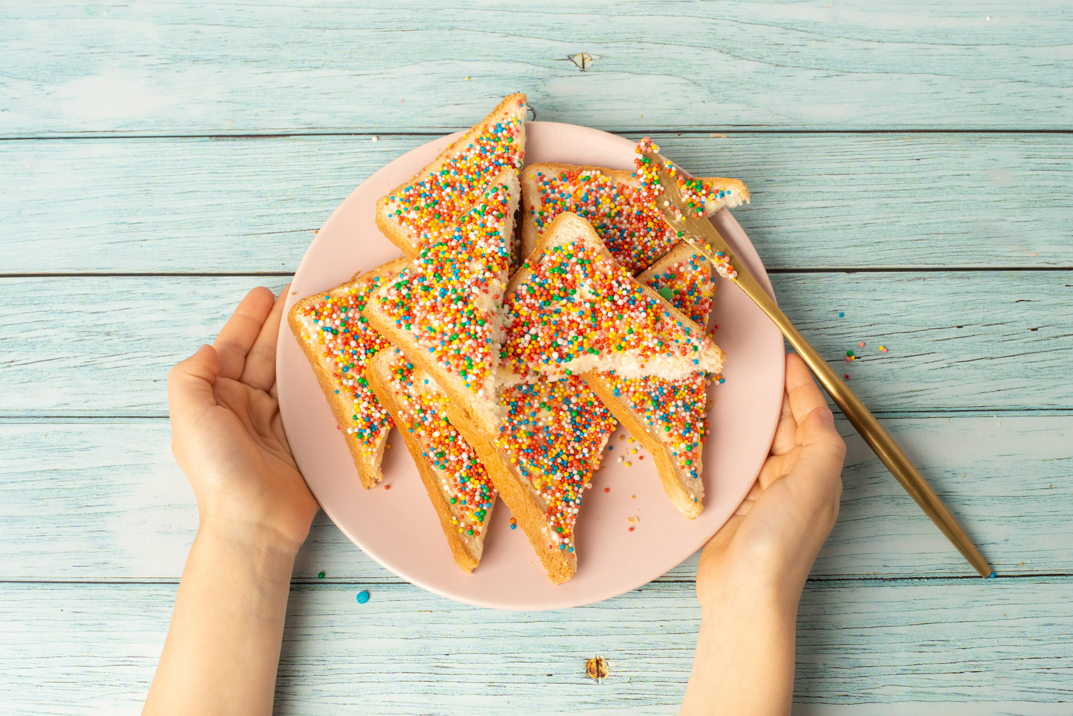 A plate of triangle-shaped cookies with white icing and colorful sprinkles, held on both sides by two hands. A gold star-shaped cookie cutter is on the plate