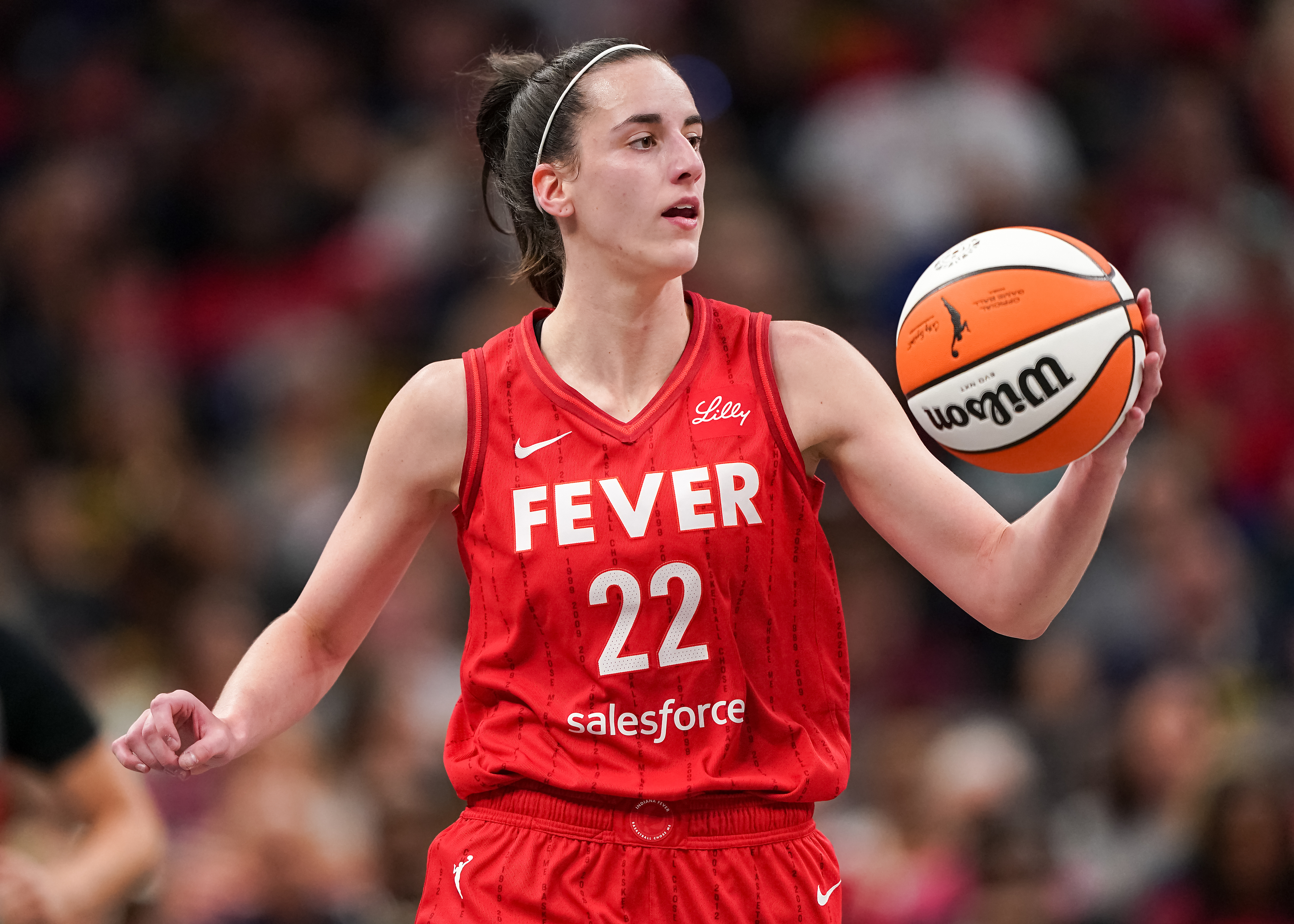 Kelsey Mitchell is playing basketball in a red Fever jersey, holding a basketball