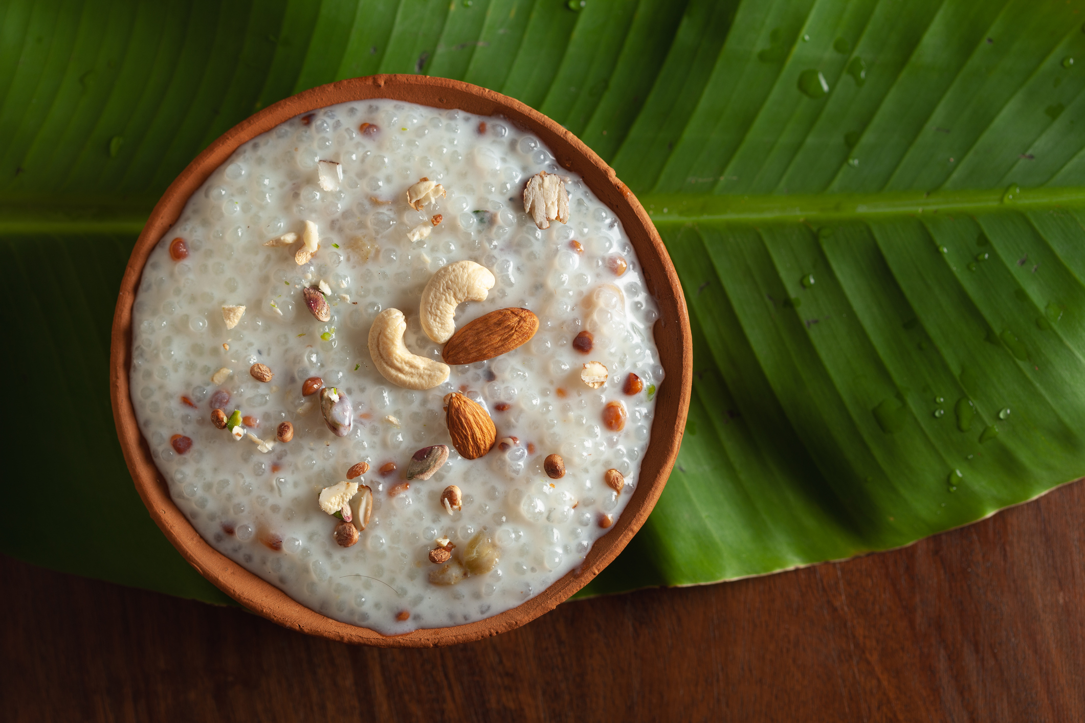 A bowl of tapioca pudding topped with nuts, placed on a large green leaf