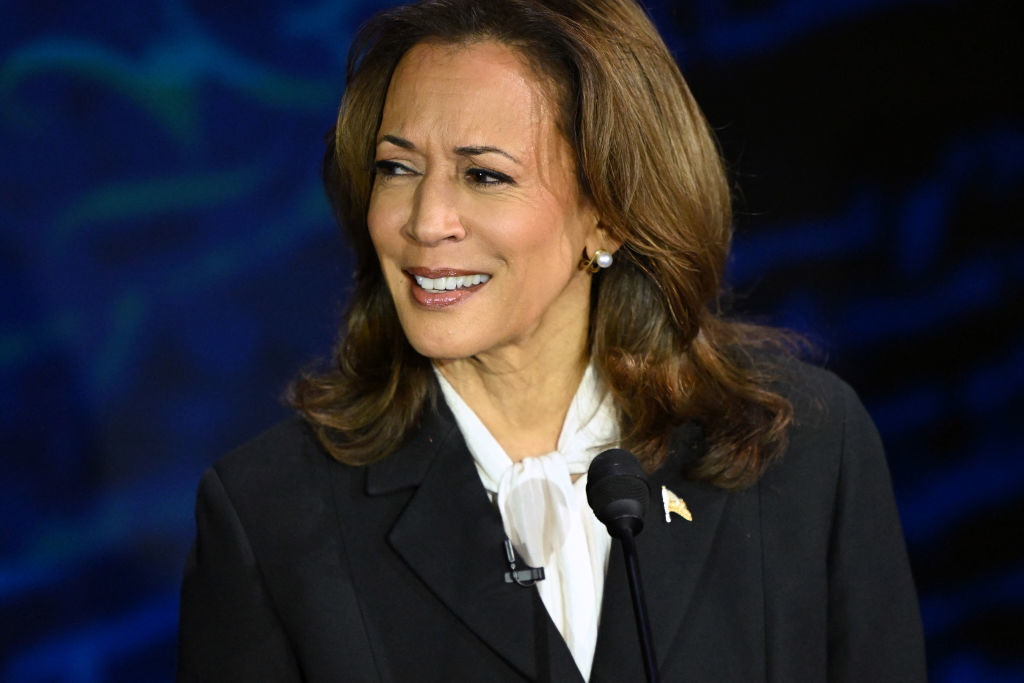 Kamala Harris, wearing a dark suit with a white blouse, smiles while speaking at a podium