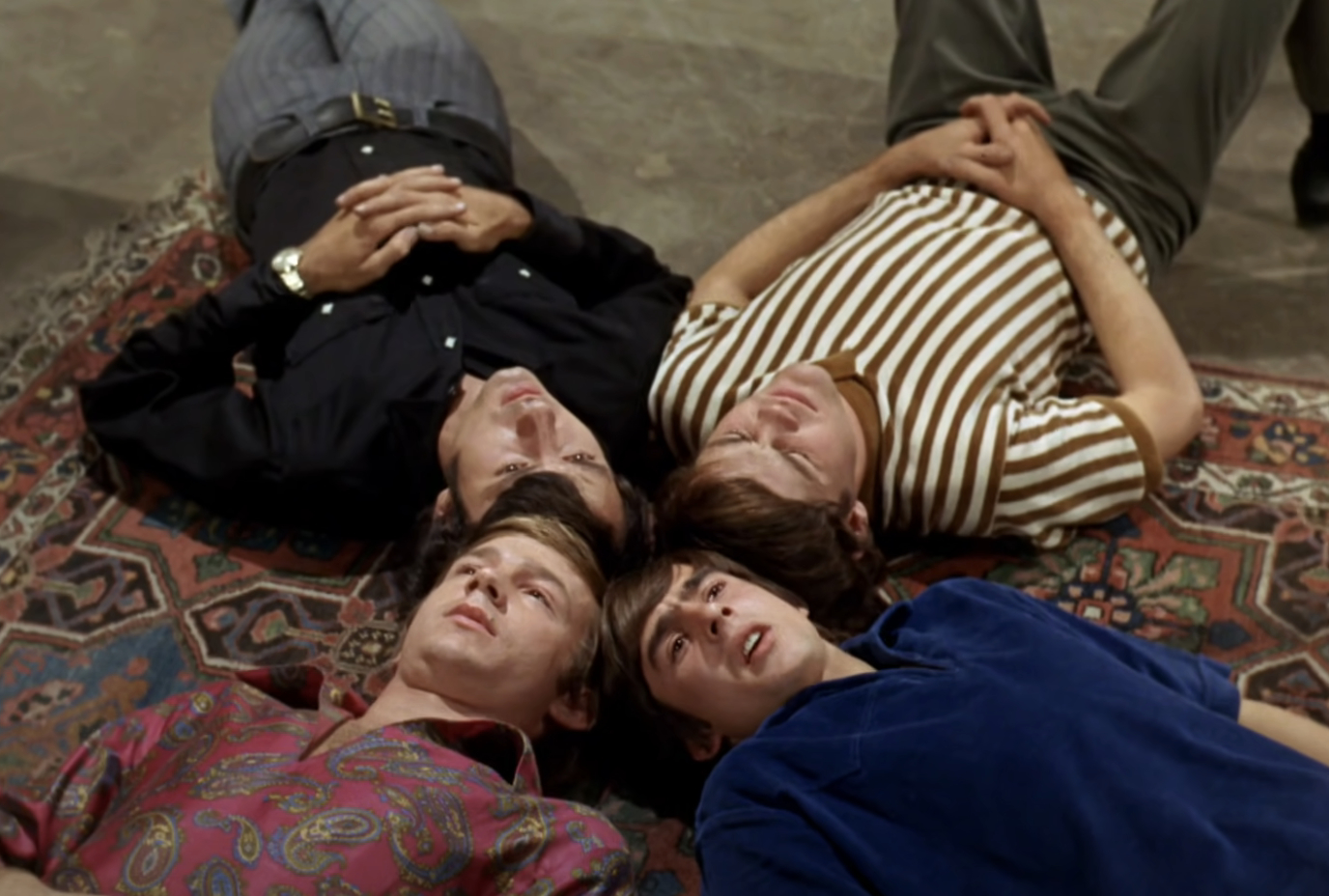 Micky Dolenz, Michael Nesmith, Peter Tork, and Davy Jones of The Monkees lay on a rug with heads together, looking upward