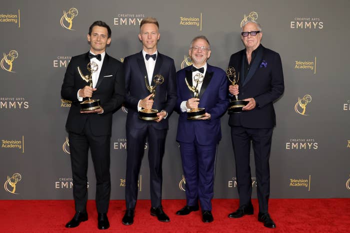 Only Murders in the Building creators on a red carpet holding Emmy Awards, all wearing suits