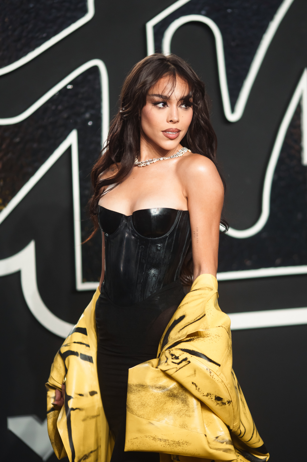 Madison Beer en un evento, lleva un corsé negro con un abrigo amarillo colgado de los hombros