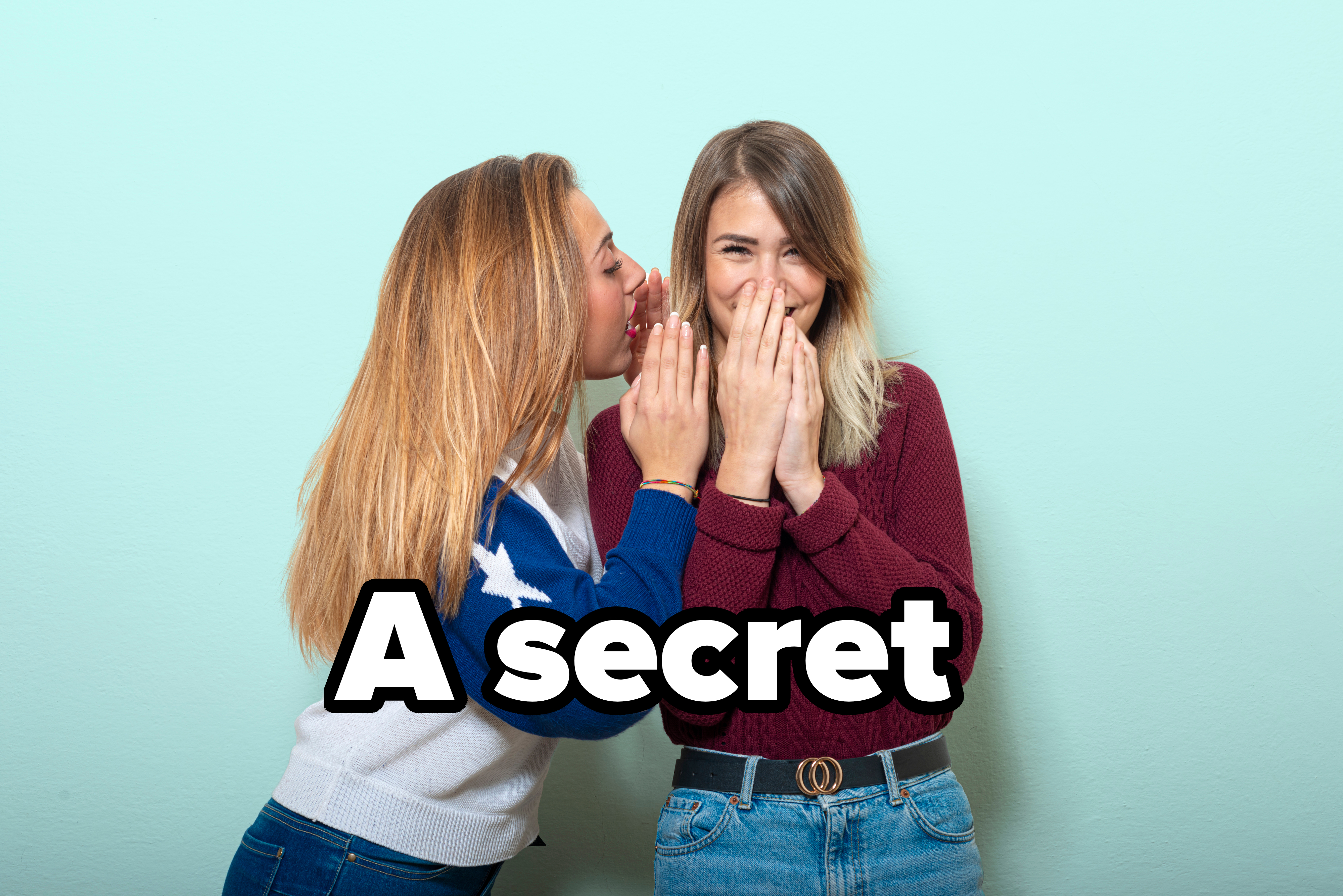 Two women, one wearing a star-patterned sweater and the other in a maroon top with a black belt, share a secret, smiling and laughing