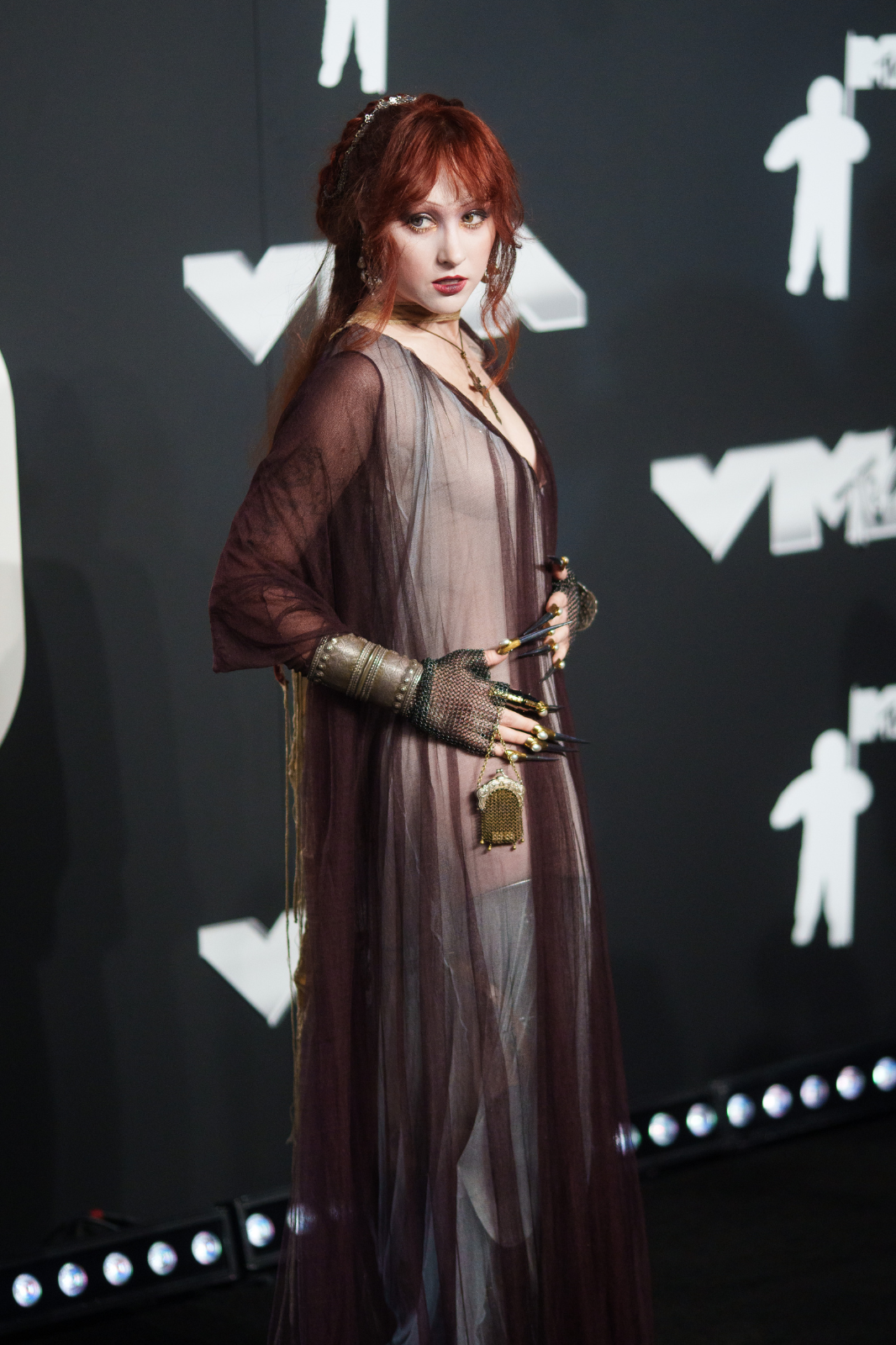 Bella Poarch en la alfombra del evento MTV. Lleva un vestido transparente, decorado con accesorios metálicos en sus manos y brazos