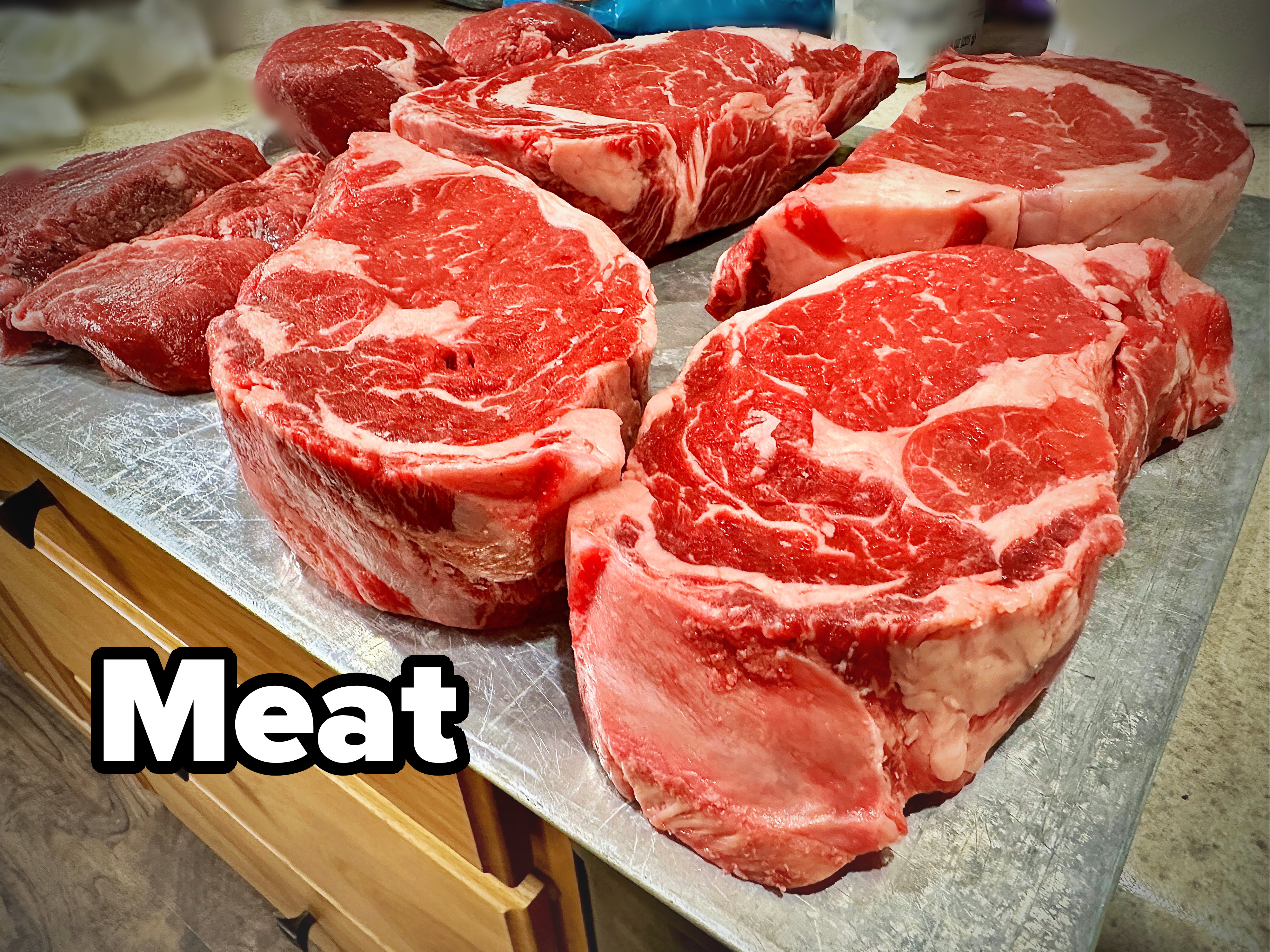 Thick, marbled ribeye steaks are displayed on a countertop, ready for cooking